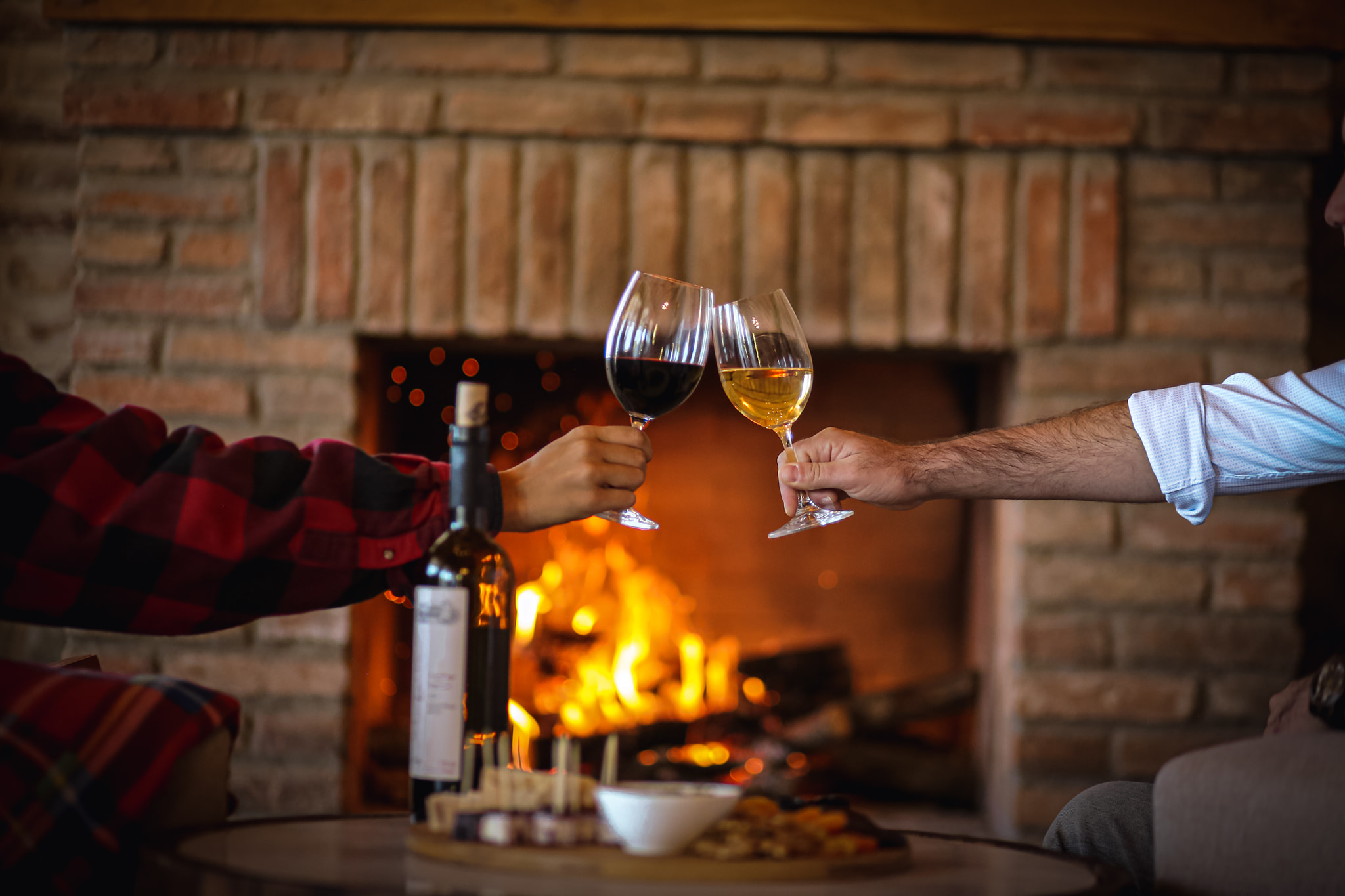 Zwei Personen stoßen mit Gläsern Schuchmann-Wein an, vor dem warmen Schein eines Kaminfeuers