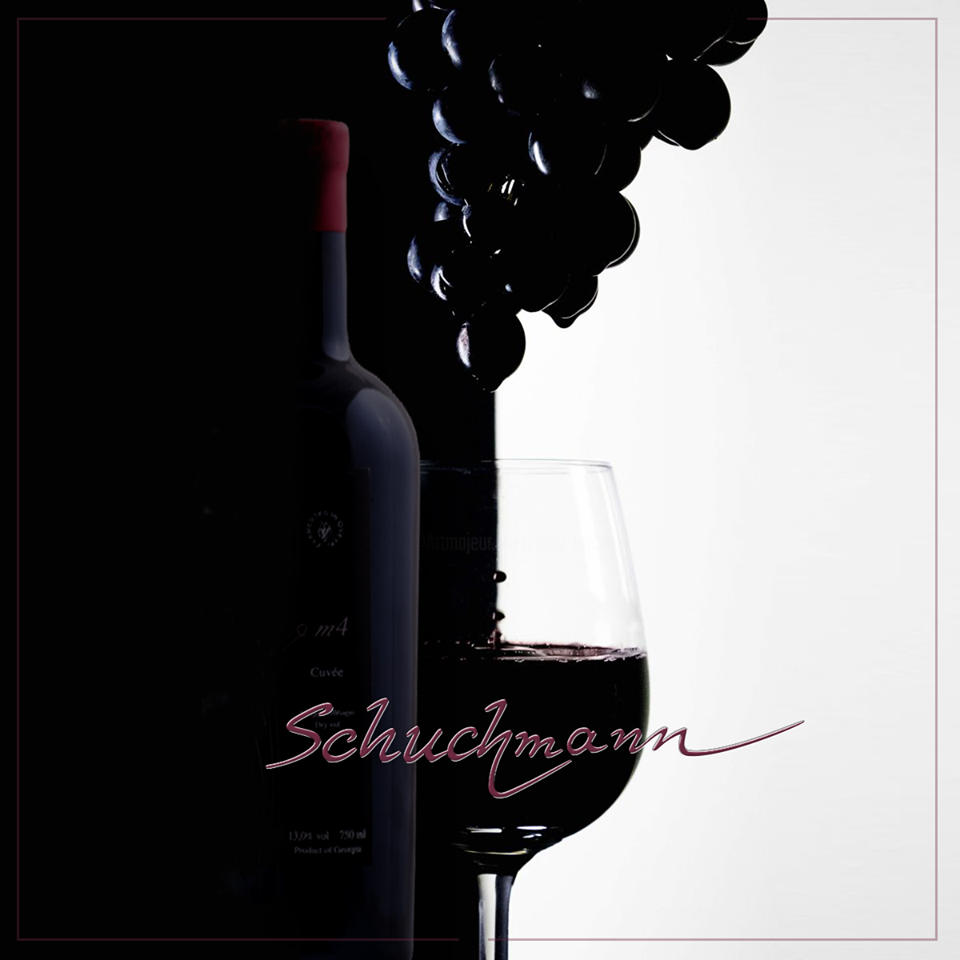 Silhouette einer Schuchmann-Weinflasche und eines gefüllten Glases vor einer Traubenreihe auf hellem Hintergrund.